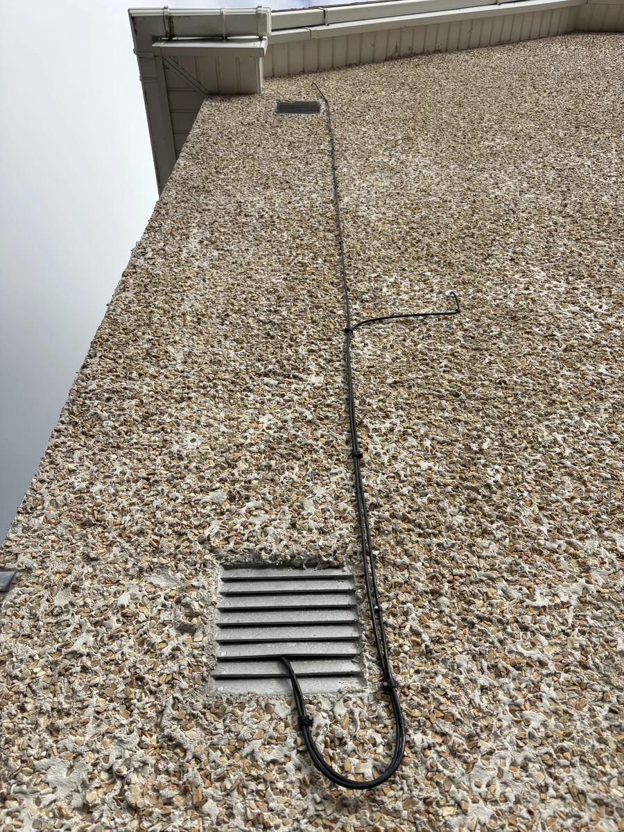 External cable route running down the rendered wall and beneath the eaves at Niall’s home